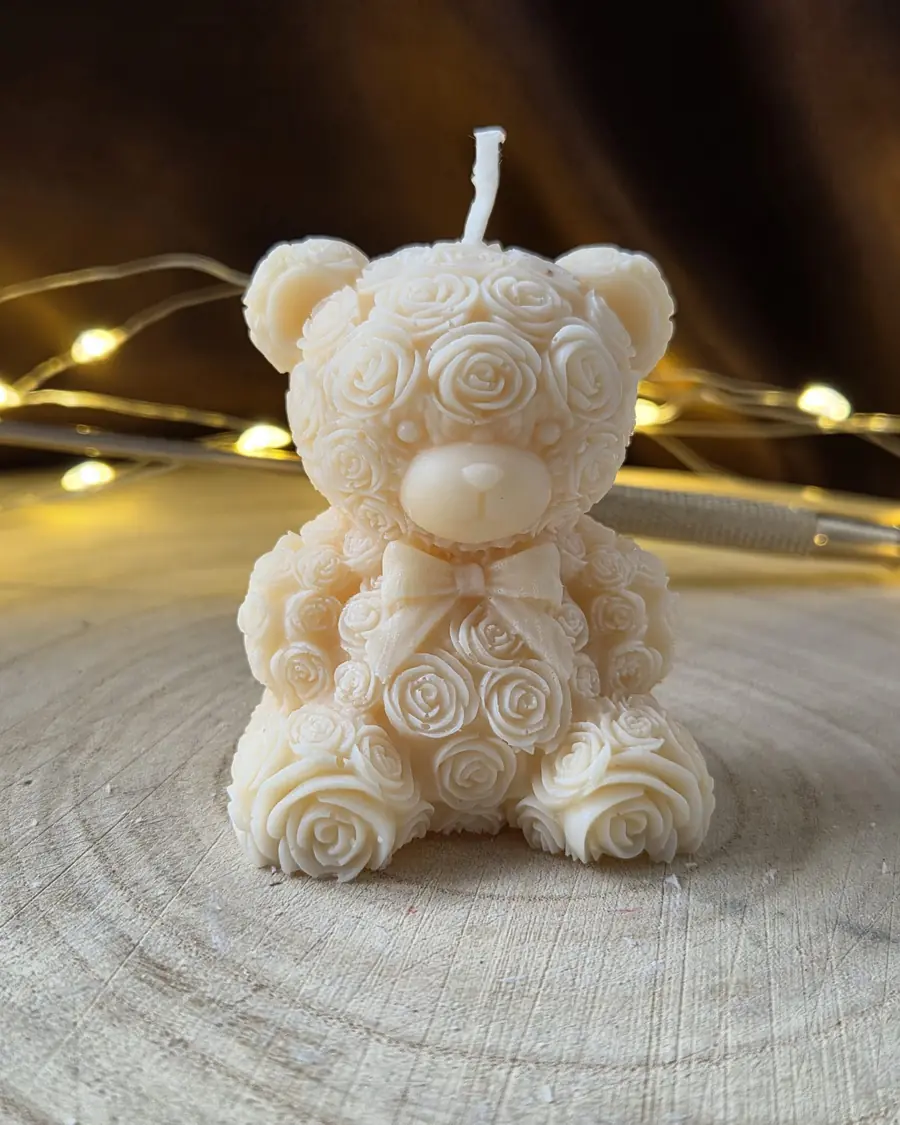 Ivory teddy bear candle covered in moulded roses with a bow, on a wood slice